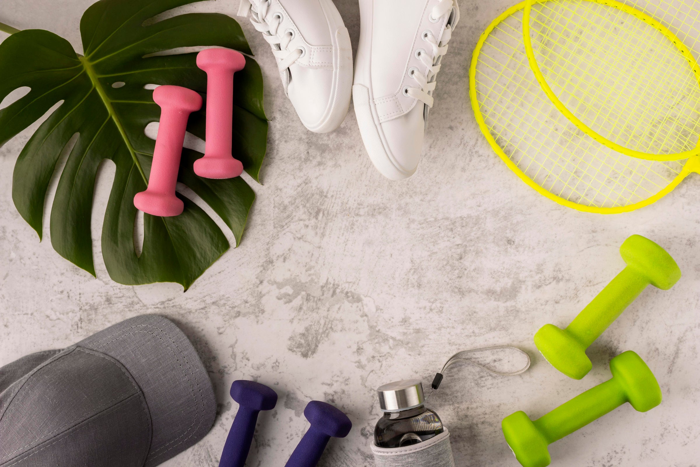 Fitness items including dumbbells, a cap, and a racket on a light surface with a leaf.